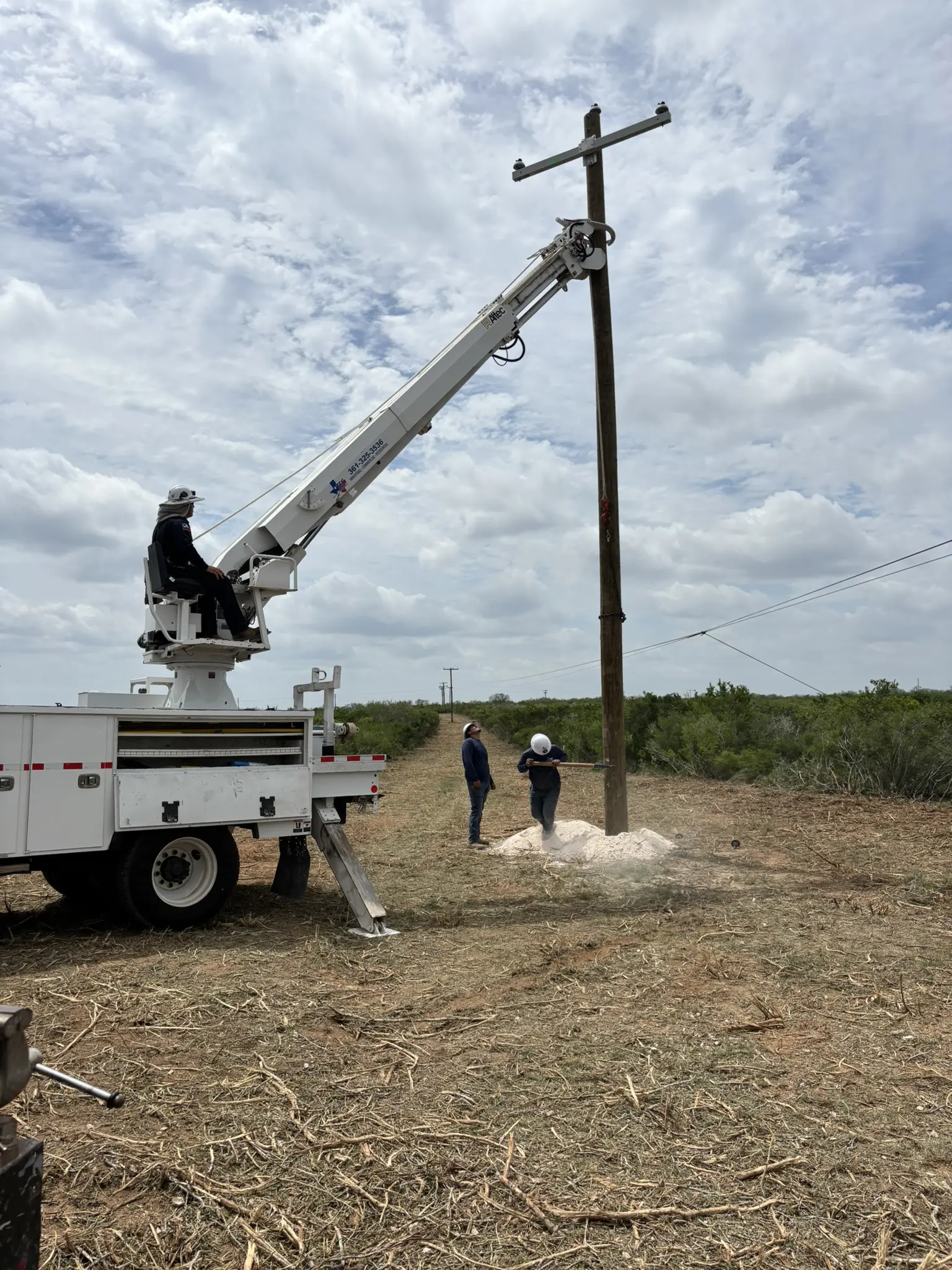 Workers installing utility pole with crane truck.